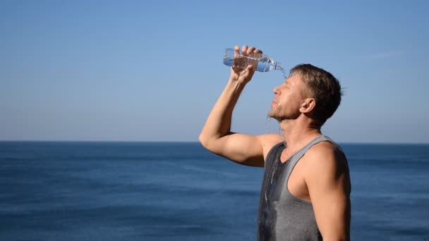 一个男人从海洋上的塑料瓶子里向他的脸上泼水 锻炼后提神 — 图库视频影像