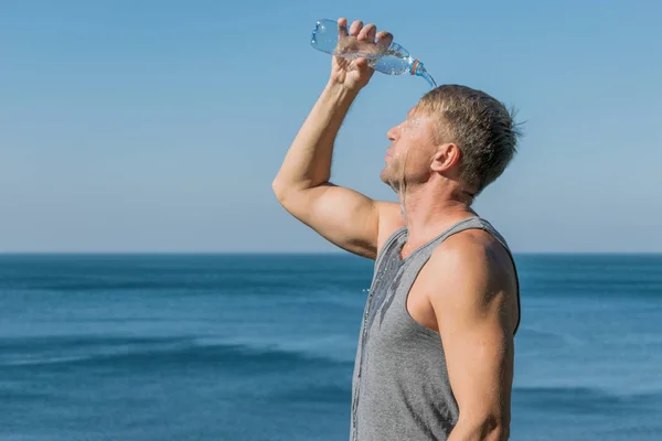 A man pours water on his face from a plastic bottle on the ocean