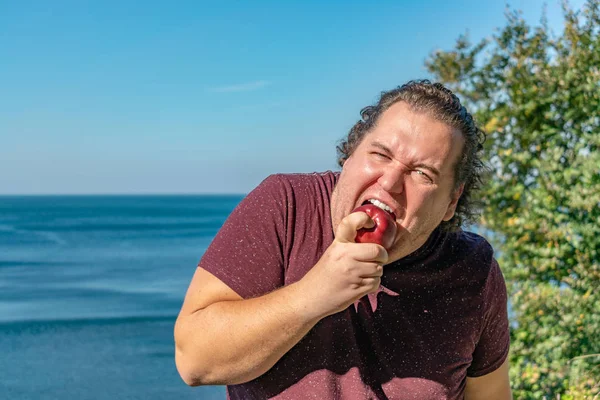 Funny fat man on the ocean eating fruits