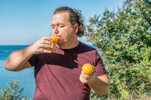Hombre gordo divertido en el océano bebiendo jugo y comiendo frutas. Vacaciones, pérdida de peso y alimentación saludable —  Fotos de Stock