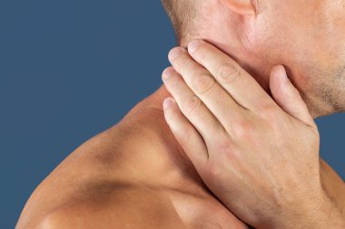 Acı çeken, üzerinde mavi arka plan izole boynunu tutan adam. Alt boyun ağrısı. Gömleksiz adam boynu ağrı için dokunaklı