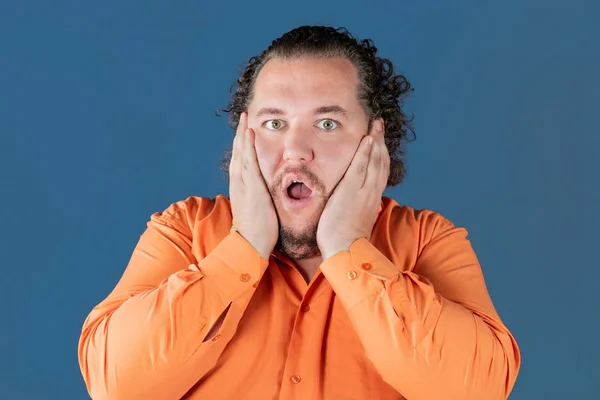 El gordo con camisa naranja sostiene sus manos sobre su cara. Está muy sorprendido. — Foto de Stock