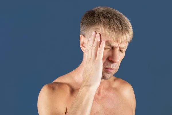 Un homme tient ses mains sur la tête sur fond bleu. Maux de tête ou migraine . — Photo