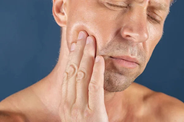 Homem triste e deprimido com dores ao segurar a bochecha. Retrato de um homem de fundo azul. emoção expressão facial. sentimentos e reação das pessoas. Dor de dente — Fotografia de Stock