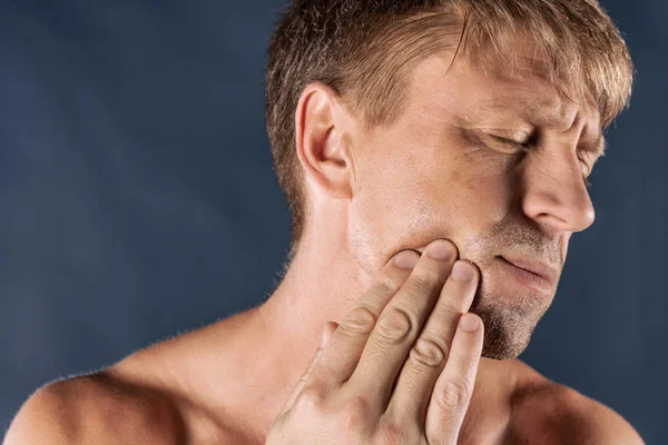 Sad depressed man in pain holding his cheek. Portrait of a man on blue background.