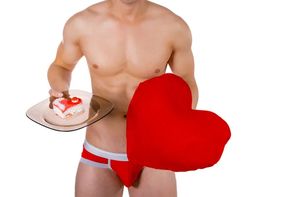 Kalp yastık ve bir plaka üzerinde kalp şeklinde pasta ile genç yakışıklı adamın gövde. Seksi beyaz izole arka planda valentine ile romantik adam portresi — Stok fotoğraf