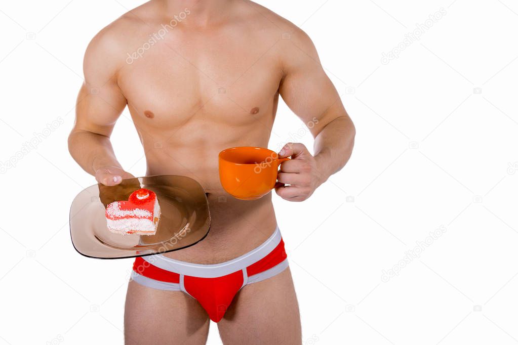 Torso of young handsome guy with orange mug and heart-shaped cake on a plate. Sexy portrait of romantic man with valentine on white isolated background