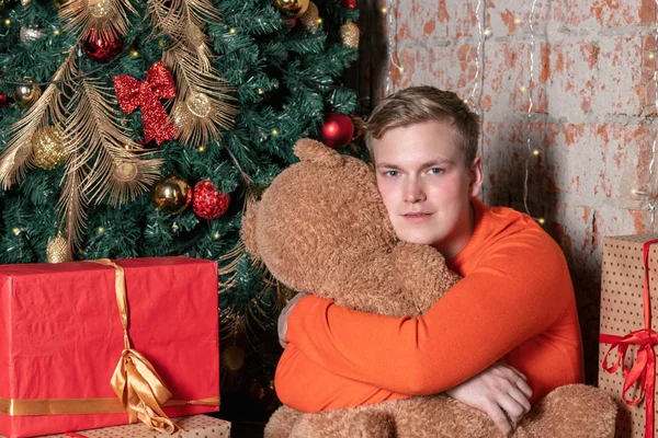 Красивый Парень Обнимает Медведя Сидящего Деревом Окружении Подарков — стоковое фото