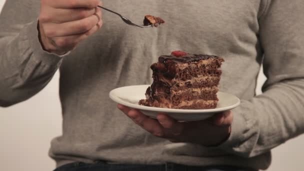 Человек в свитере ест большой кусок шоколадного торта — стоковое видео