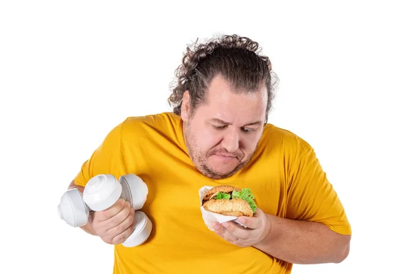 Hombre gordo divertido comiendo alimentos poco saludables y tratando de hacer ejercicio aislado sobre fondo blanco — Foto de Stock
