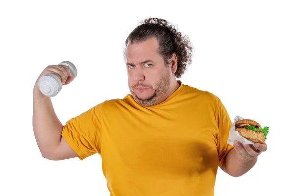 Hombre gordo divertido comiendo alimentos poco saludables y tratando de hacer ejercicio aislado sobre fondo blanco — Foto de Stock