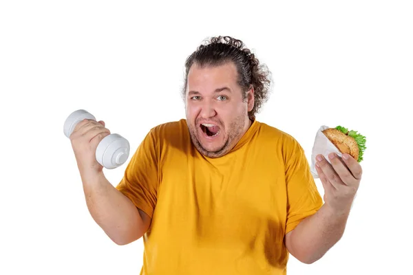 Hombre gordo divertido comiendo alimentos poco saludables y tratando de hacer ejercicio aislado sobre fondo blanco — Foto de Stock