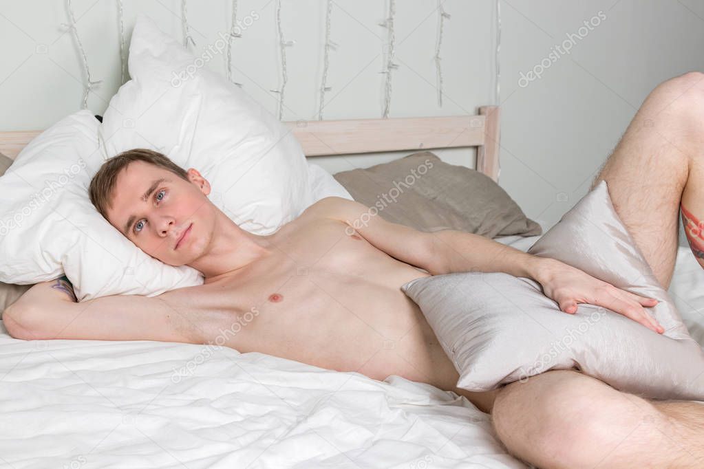 Handsome young adult man sleeping in bed. Sexy naked guy is resting