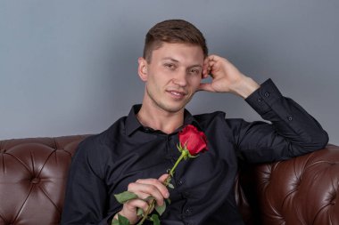 Siyah gömlek giyen yakışıklı adam bir gül tutan deri kanepede oturan ve romantik tarih hazırlanıyor