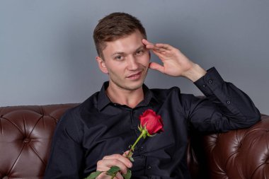 Siyah gömlek giyen yakışıklı adam bir gül tutan deri kanepede oturan ve romantik tarih hazırlanıyor