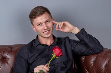 Siyah gömlek giyen yakışıklı adam bir gül tutan deri kanepede oturan ve romantik tarih hazırlanıyor