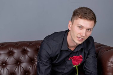 Siyah gömlek giyen yakışıklı adam bir gül tutan deri kanepede oturan ve romantik tarih hazırlanıyor