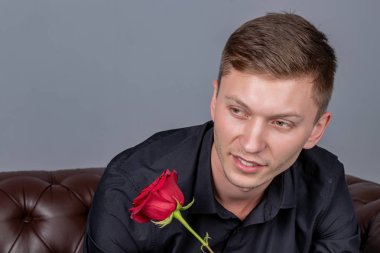 Siyah gömlek giyen yakışıklı adam bir gül tutan deri kanepede oturan ve romantik tarih hazırlanıyor