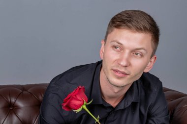 Siyah gömlek giyen yakışıklı adam bir gül tutan deri kanepede oturan ve romantik tarih hazırlanıyor