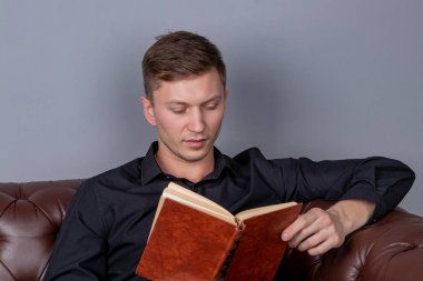 Genç adam deri koltukta oturuyor ve kitap okuyor.