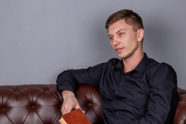 Genç adam deri koltukta oturuyor ve kitap okuyor.