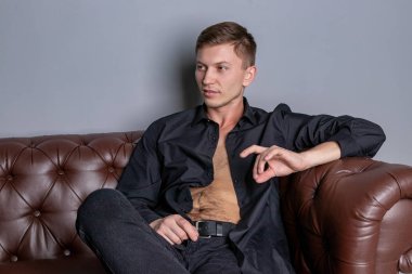 Deri kanepede oturan siyah gömlek giyen seksi yakışıklı adam. Konfor ve rahatlama