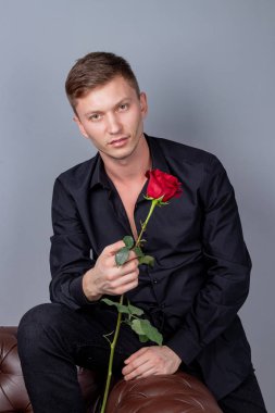 Siyah gömlek giyen yakışıklı adam bir gül tutan deri kanepede oturan ve romantik tarih hazırlanıyor