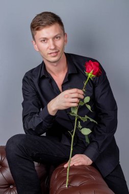 Siyah gömlek giyen yakışıklı adam bir gül tutan deri kanepede oturan ve romantik tarih hazırlanıyor