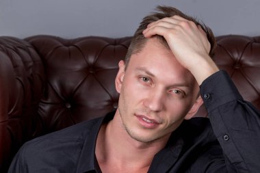 Deri kanepe yakınında katta oturan siyah gömlek giyen seksi yakışıklı adam. Konfor ve rahatlama