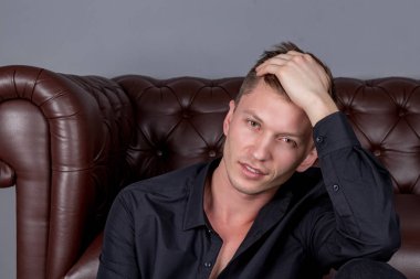 Deri kanepe yakınında katta oturan siyah gömlek giyen seksi yakışıklı adam. Konfor ve rahatlama