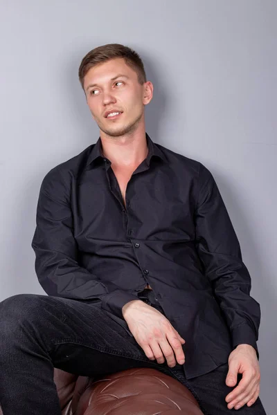 Sexy pohledný muž na černé košili, sedící na kožené pohovce. Pohodlí a relaxace — Stock fotografie
