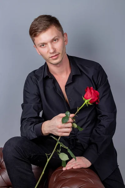 Pohledný muž na černé košili, sedící na kožené pohovce s růžovou a připravenej Romantický rande — Stock fotografie