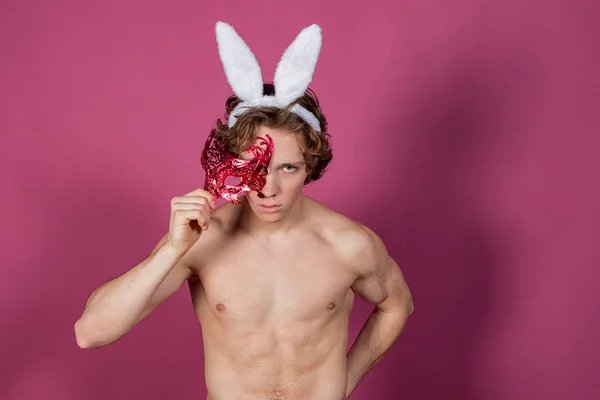 Srandovní chlapík s králíčkem a karnevalovou maskou na růžovém pozadí — Stock fotografie