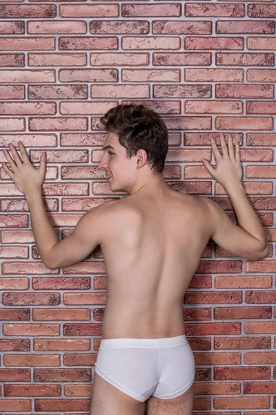 Junge nackte sexy Kerl posiert in Unterwäsche auf dem Hintergrund einer Ziegelwand — Stockfoto