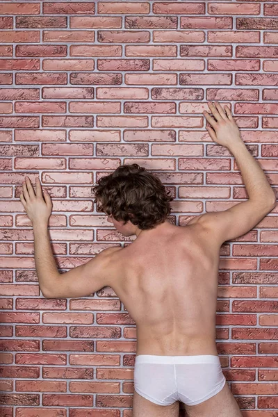 Mladý nahý sexy chlap pózuje ve spodním prádle na pozadí cihlové zdi — Stock fotografie