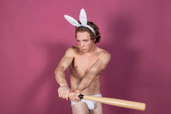 Смішний голий хлопець у кролячих вухах з бейсбольною битою на рожевому фоні — стокове фото