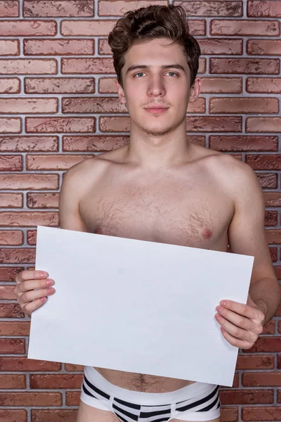 Joven chico sexy desnuda posando en ropa interior con una cartelera en el fondo de una pared de ladrillo —  Fotos de Stock