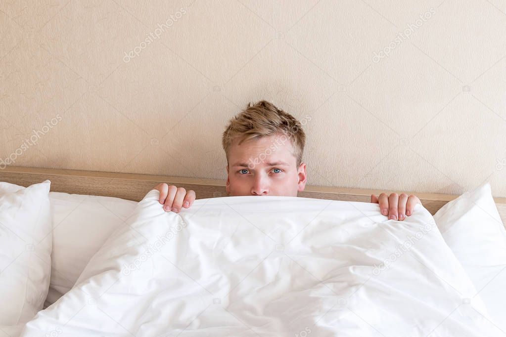 Funny guy in bed under the blanket after sleeping. Sleepy man waking up