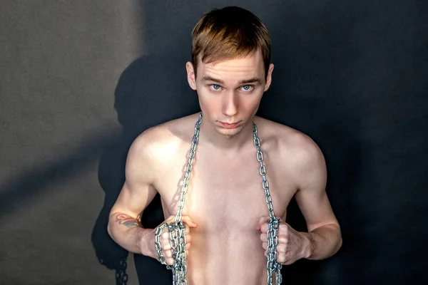 Handsome skinny guy holding a chain. Black background