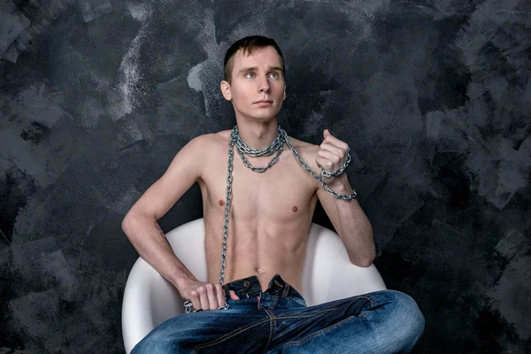 Handsome skinny guy holding a chain. Black background