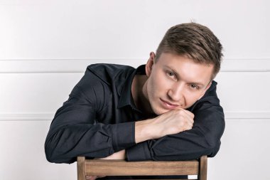 Siyah gömlekli pensive genç yakışıklı adam sandalyede oturan ve kameraya bakarak