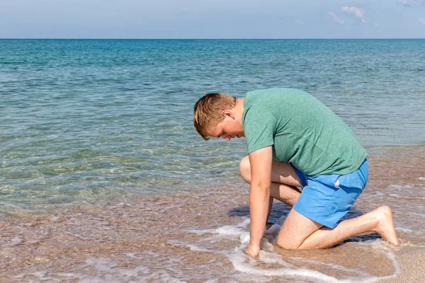 Hombre joven en una camiseta en la orilla del mar y mira al mar, vista trasera —  Fotos de Stock