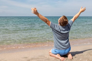 Sahilde oturan bir t-shirt mutlu genç adam ve denize bakıyor, arka görünüm
