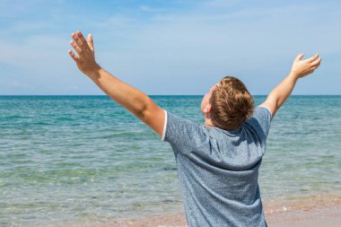 Sahilde oturan bir t-shirt mutlu genç adam ve denize bakıyor, arka görünüm