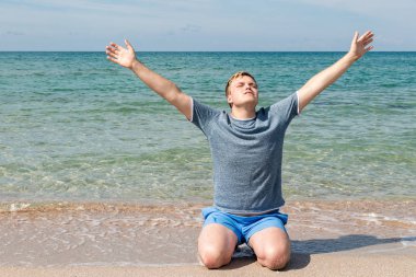 Sahilde oturan bir t-shirt mutlu genç adam ve denize bakıyor, arka görünüm