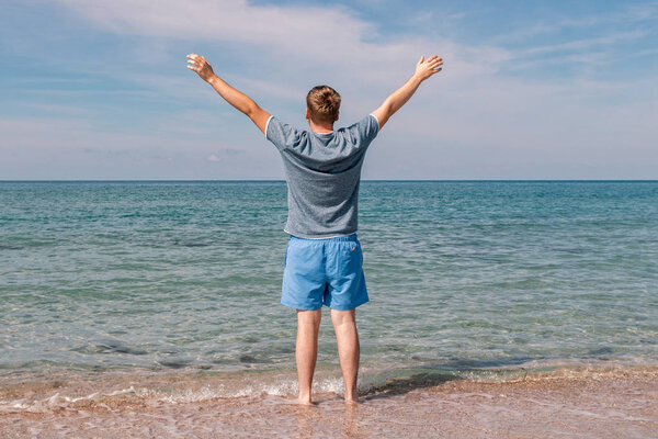 Young man in a t-shirt on the seashore and looks at the sea, back view