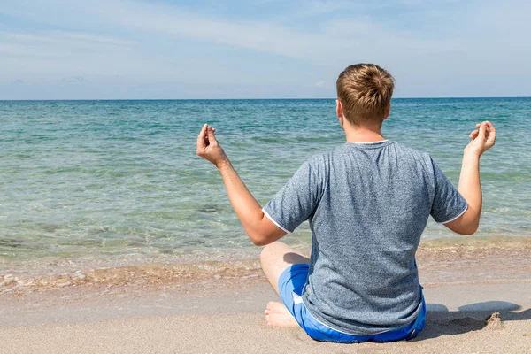 Jovem feliz sentado com as pernas cruzadas na praia. Yoga e fitness — Fotografia de Stock