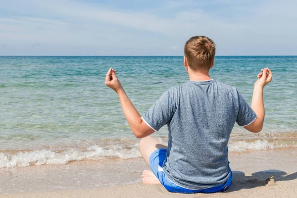 Plajda bacaklarla oturan mutlu genç adam. Yoga ve Fitness