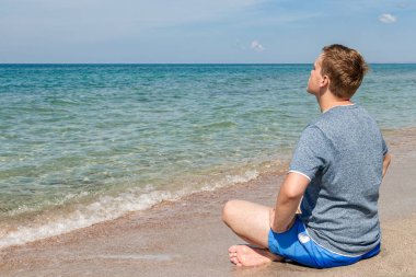 Plajda bacaklarla oturan mutlu genç adam. Yoga ve Fitness