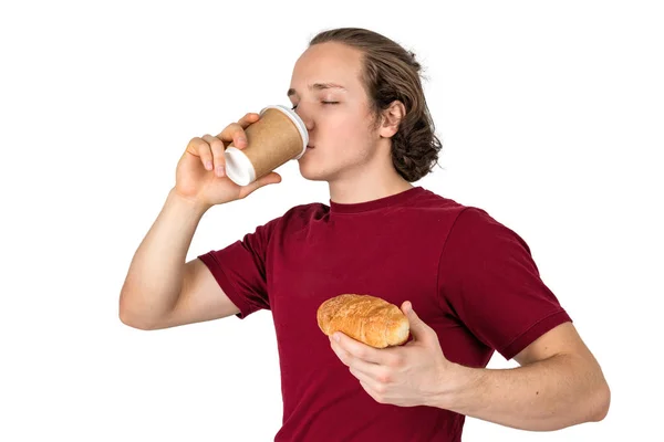 Jovem bonitão bebe café e come croissant. Café da manhã francês e café da manhã. Isolados — Fotografia de Stock